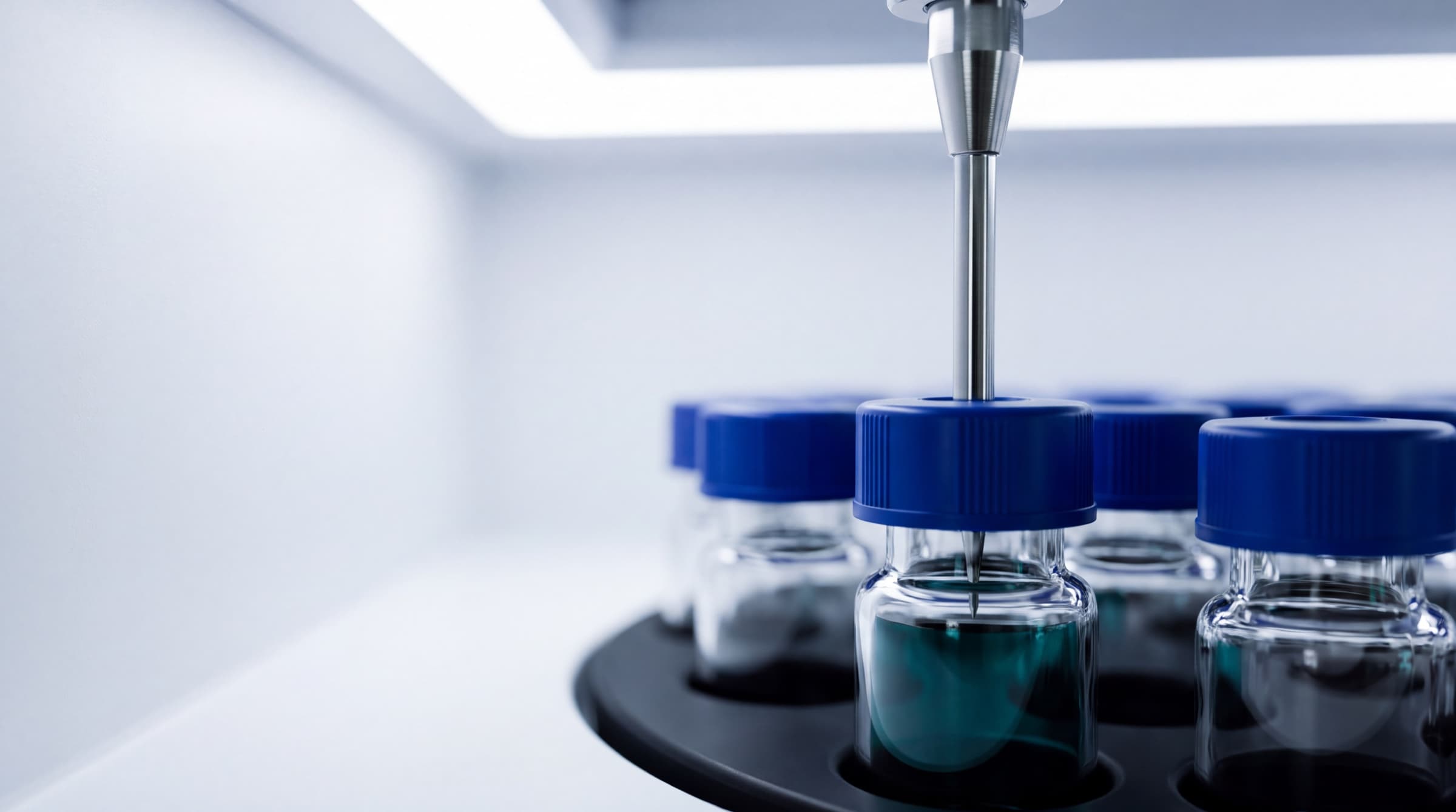 Illustration: an HPLC autosampler needle poised over one blue-capped 2 mL vial, with the rest of the run in rows behind it.